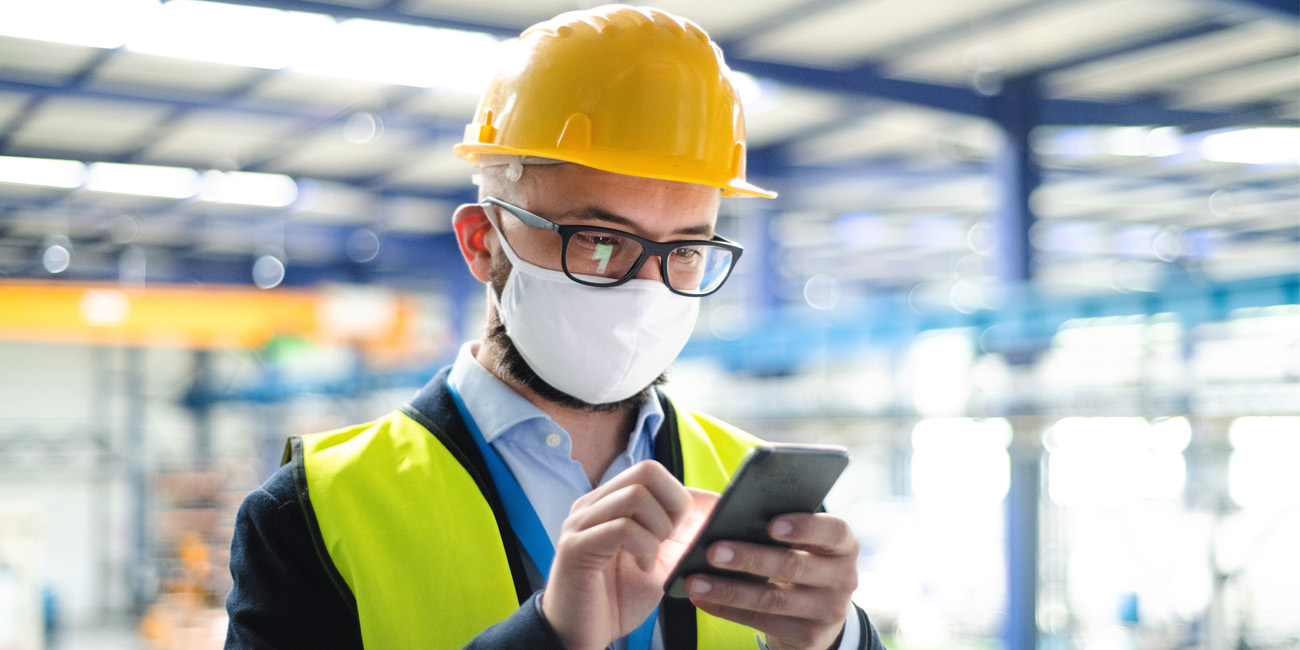 Technician wearing protective mask and hardhat checking his mobile device for an alert