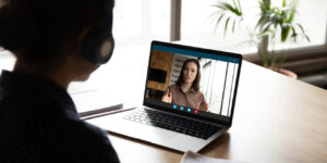 Employer on laptop screen conducting performance review while the employee listens and takes notes