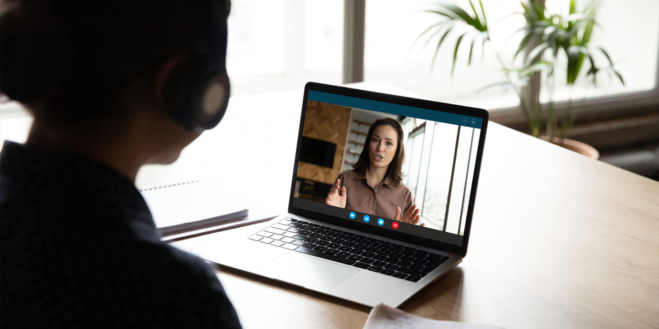 Employer on laptop screen conducting performance review while the employee listens and takes notes